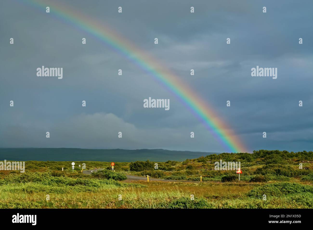 Einsame Straße durch die wunderschöne grüne landschaft islands nach Regenwetterwechsel mit bunten Regenbogen - Island Stockfoto