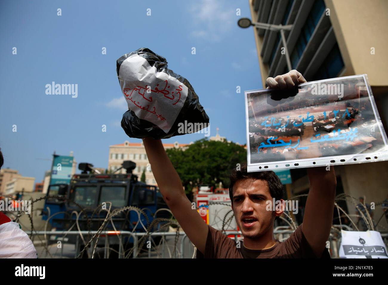 A Lebanese protester holds up a trash bag and a placard with Arabic