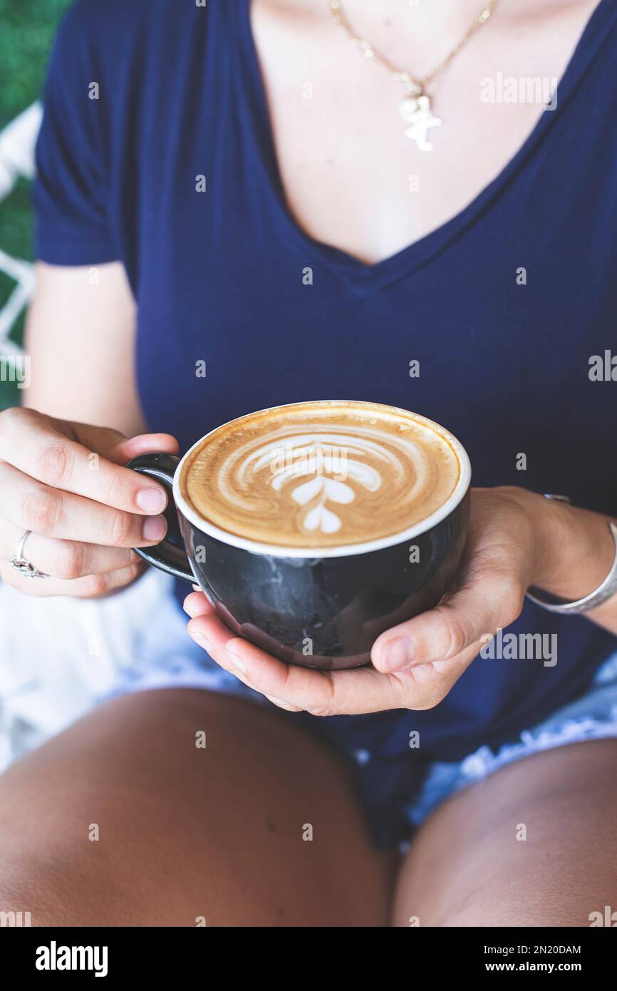 Frauenhände halten eine Tasse Kaffee, die von einem Barista zubereitet wurde. Restaurant. Ruhige Atmosphäre. Stockfoto