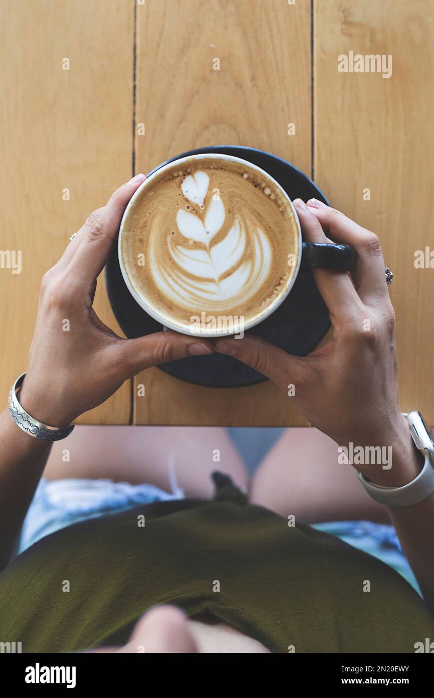 Frauenhände halten eine Tasse Kaffee, die von einem Barista zubereitet wurde. Restaurant. Ruhige Atmosphäre. Stockfoto