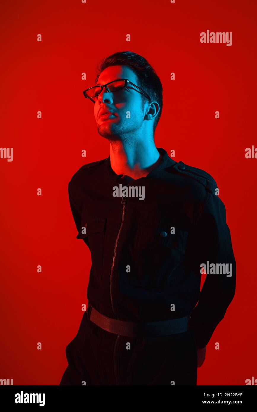 Studioporträt eines attraktiven, modischen jungen weißen Brünetten, der eine Brille in einem stilvollen Overall mit leuchtendem Neonrot trägt Stockfoto