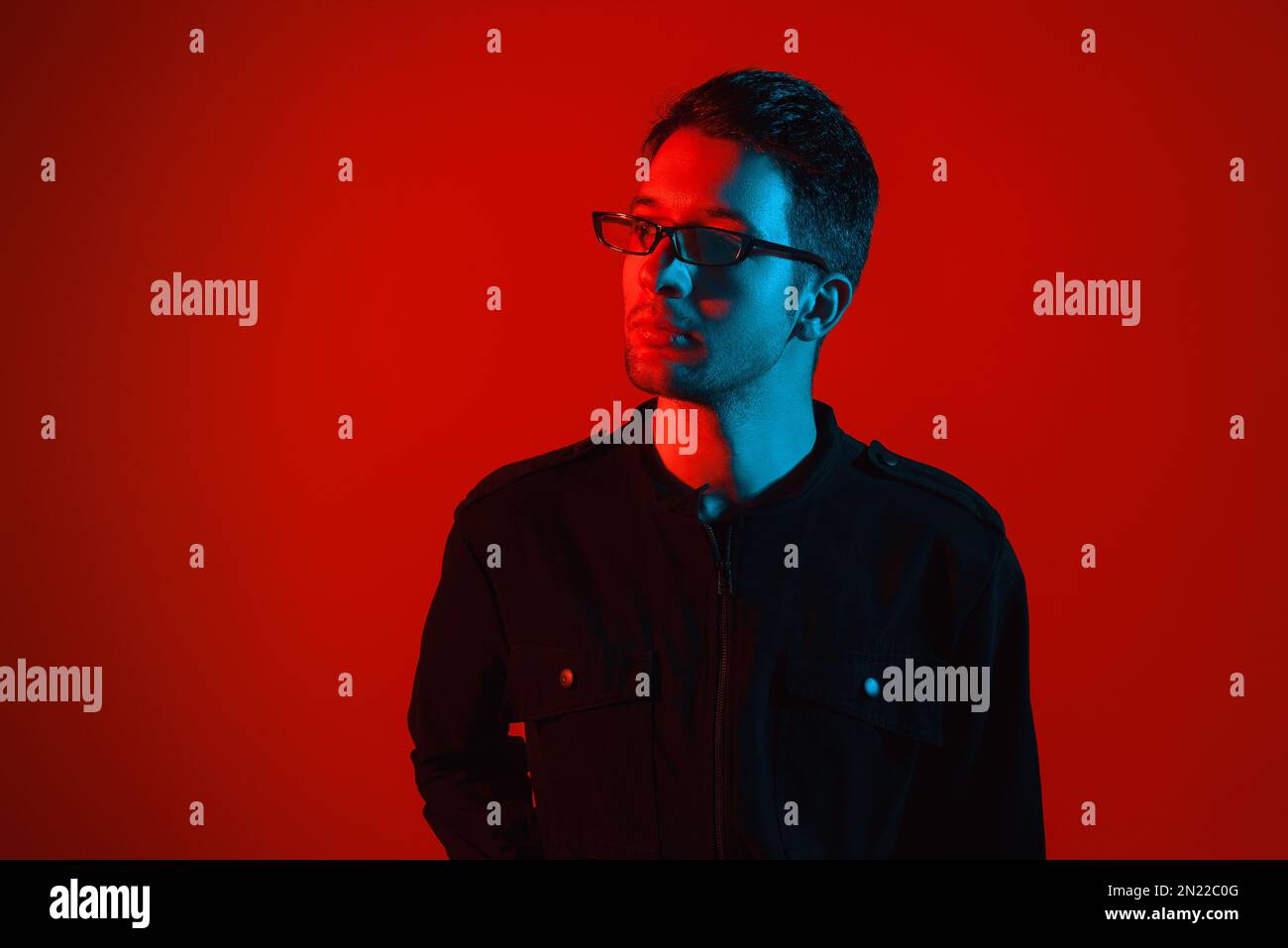 Studioporträt eines attraktiven, modischen jungen weißen Brünetten, der eine Brille in einem stilvollen Overall mit leuchtendem Neonrot trägt Stockfoto