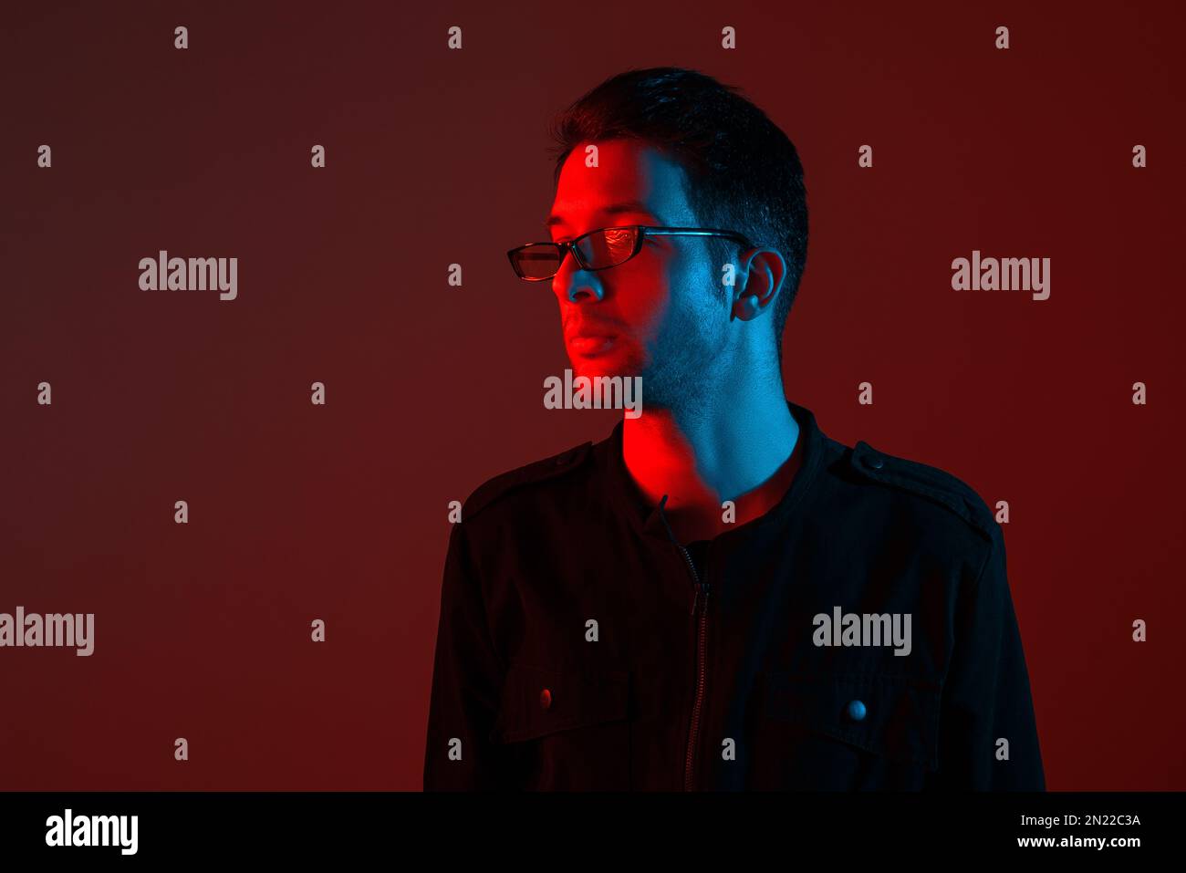 Studioporträt eines attraktiven, modischen jungen weißen Brünetten, der eine Brille in einem stilvollen Overall mit leuchtendem Neonrot trägt Stockfoto