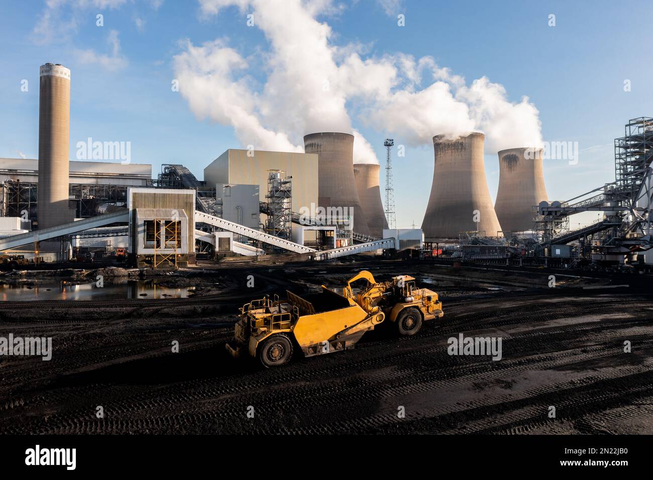 Ein schweres Kraftwerk, das Kohle aus einem fossilen Brennstoffstapel in einem großen Kohlekraftwerk abkratzt, um nicht erneuerbare Energie zu erzeugen Stockfoto