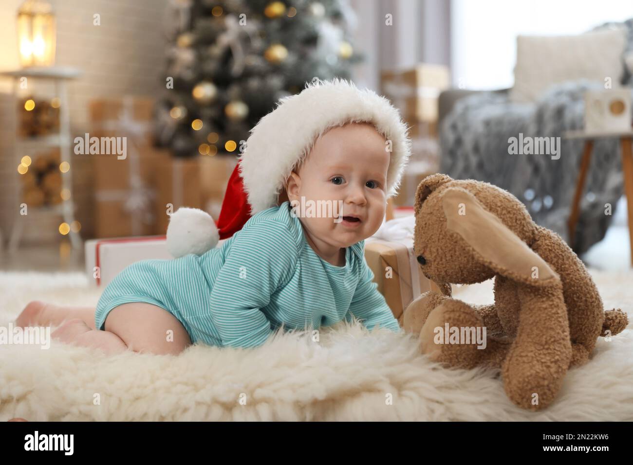 Süßes Baby mit Weihnachtsmannmütze, das auf dem Boden krabbelt. Erstes Weihnachten Stockfoto