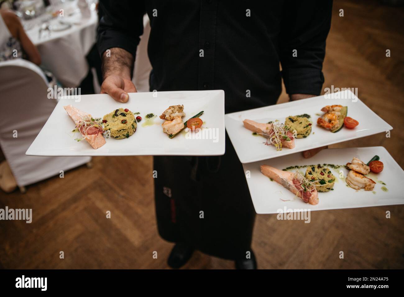 Ein Kellner, der das Fischgericht auf Keramiktellern serviert hat, auf einer Party Stockfoto