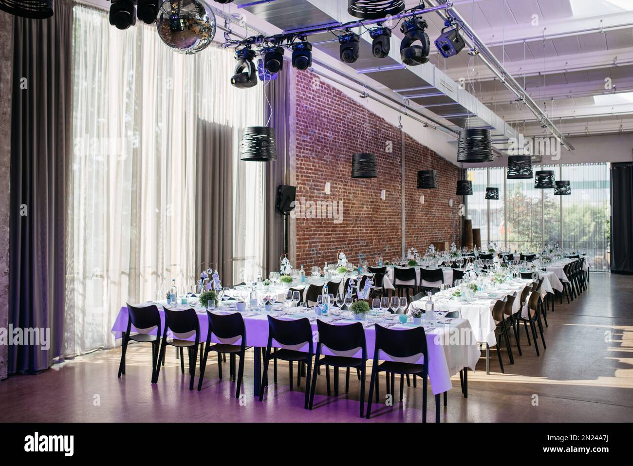Ein romantisch eingerichteter Hochzeitssaal mit Tischdecken für die Hochzeitsfeier und farbenfrohen Lichtreflektoren an der Decke Stockfoto