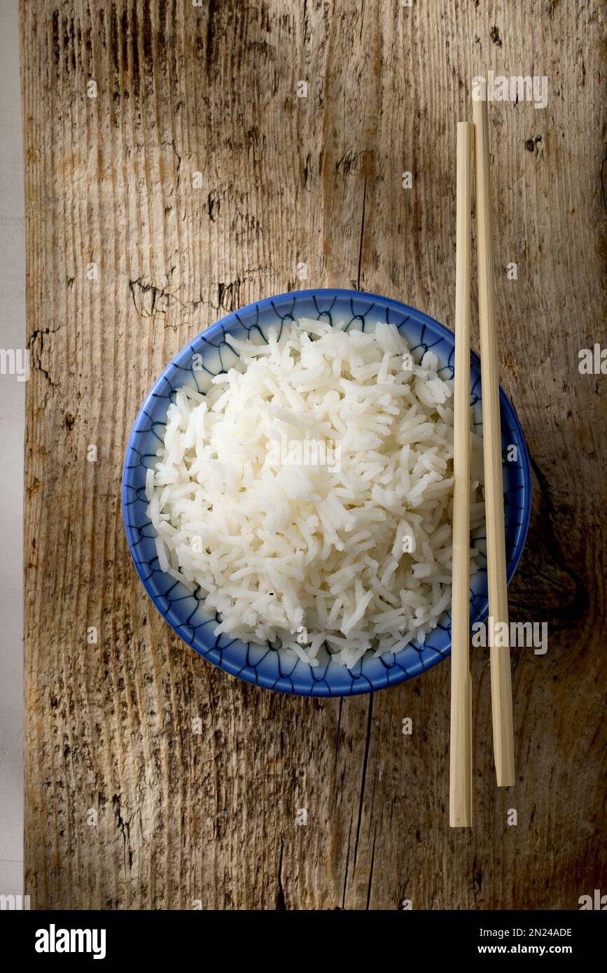 Schüssel mit gekochtem Reis und Essstäbchen auf einem hölzernen Küchentisch, Draufsicht Stockfoto