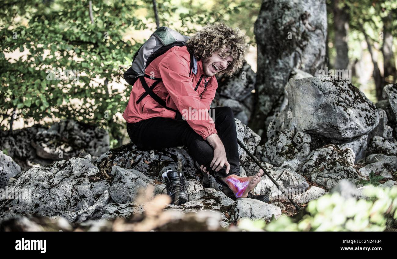 Ein Bergsteiger, der auf einem Felsen sitzt und seinen Knöchel hält. Verletzter Bergsteiger Stockfoto