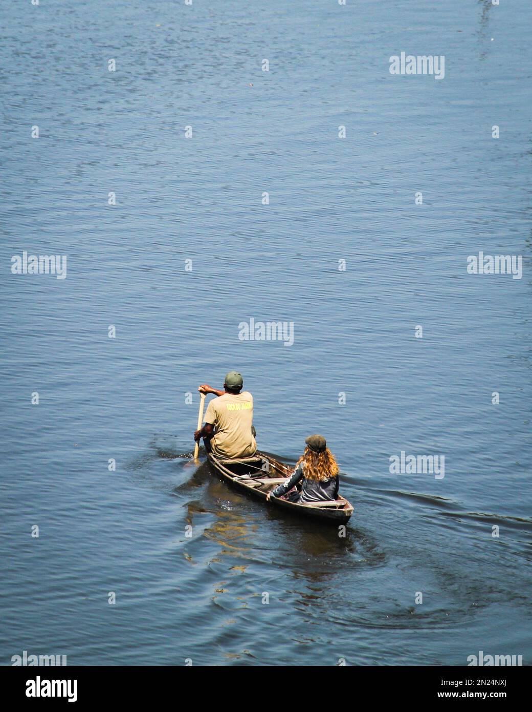 Ein vertikales Hochwinkelfoto eines Mannes, der ein Boot mit einer Touristenfrau auf dem Wasser rudert Stockfoto