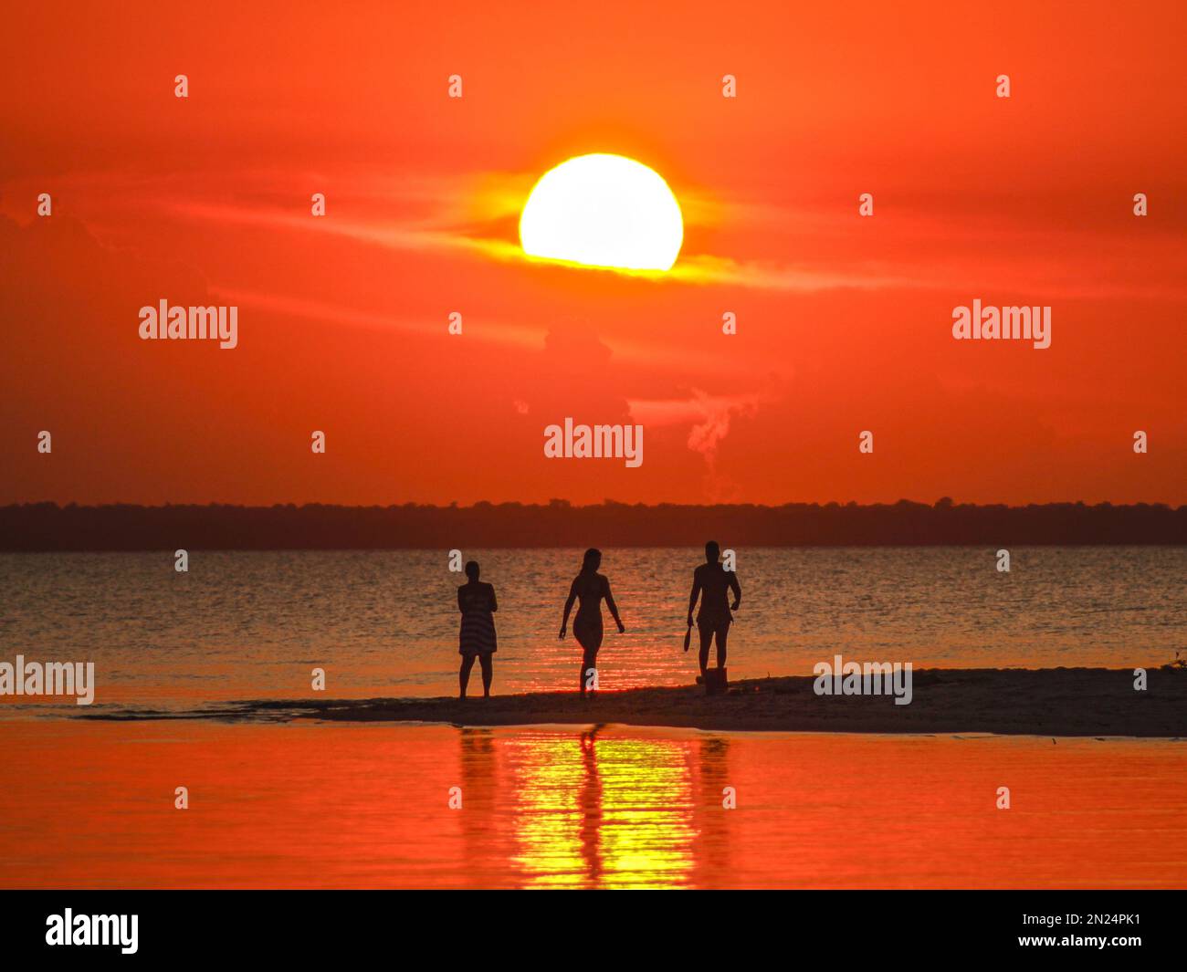 Die Silhouetten von Freunden, die bei Sonnenuntergang an der Küste spazieren Stockfoto