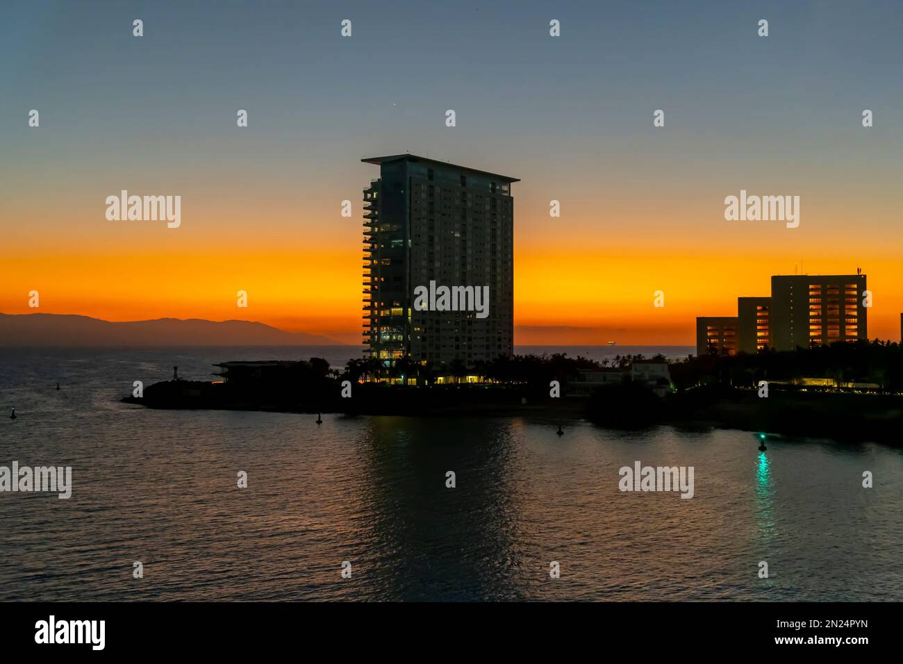Blick auf den Sonnenuntergang von einem Balkon des Kreuzfahrtschiffs auf die Skyline des Kreuzfahrthafens und das Meer, während ein Kreuzfahrtschiff in Puerto Vallarta, Mexiko, in die Ferne segelt Stockfoto