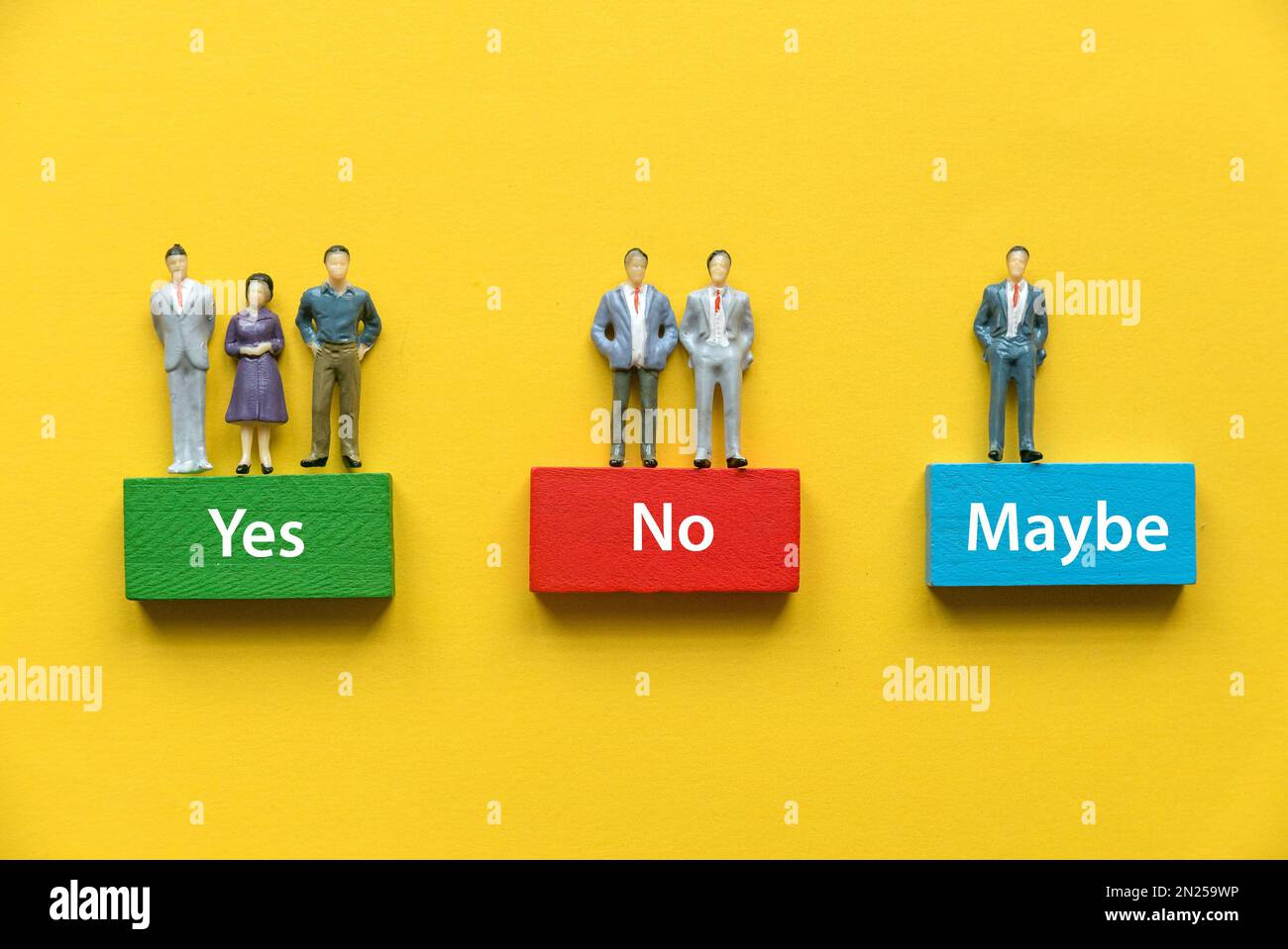 Miniaturleute, die auf einem Holzblock stehen, stellen eine Option von JA, NEIN und VIELLEICHT dar. Stockfoto