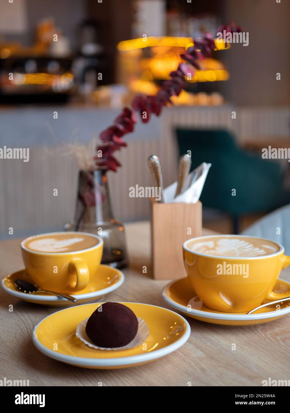 Gelbe Kaffeetassen mit Getränk und Schokoladenkuchen auf dem Tisch im Café, vertikales Format. Gemütliche Kaffeetrinken, selektive Konzentration Stockfoto