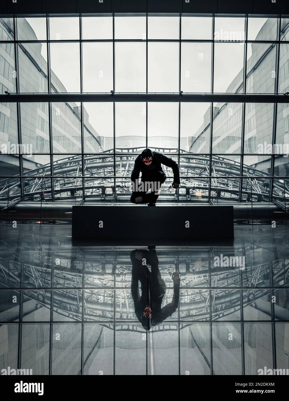 Mann mit Purge-Maske in einem modernen Gebäude, kniend und im Boden reflektiert, Frankfurt am Main, Hessen, Deutschland Stockfoto