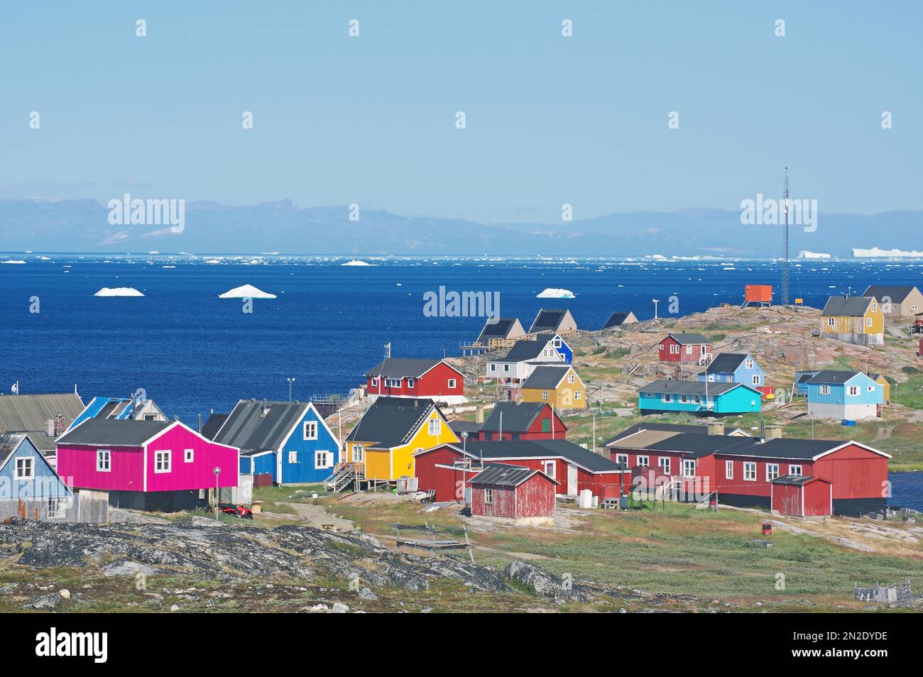 Verschiedene farbige Holzhäuser vor der Bucht mit Eisbergen, Disko Island im Hintergrund, Illimanaq, Disko Bay, Avannaata Kommunia, Arktis Stockfoto