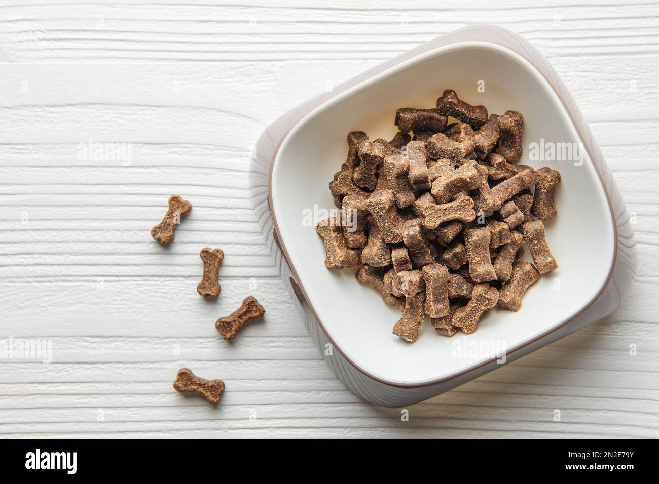 Eine Schüssel Hundefutter auf einem Holzboden. Trockenfuttergranulat in Form von Knochen. Stockfoto