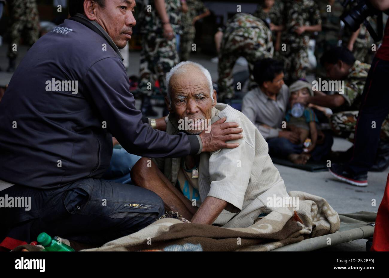 A Nepalese man attends to an elderly as victims of Saturday’s earthquake, wait for ambulances after being evacuated at the airport in Kathmandu, Nepal, Monday, April 27, 2015. The death toll from Nepal's earthquake is expected to rise depended largely on the condition of vulnerable mountain villages that rescue workers were still struggling to reach two days after the disaster. (AP Photo/Altaf Qadri) Stockfoto