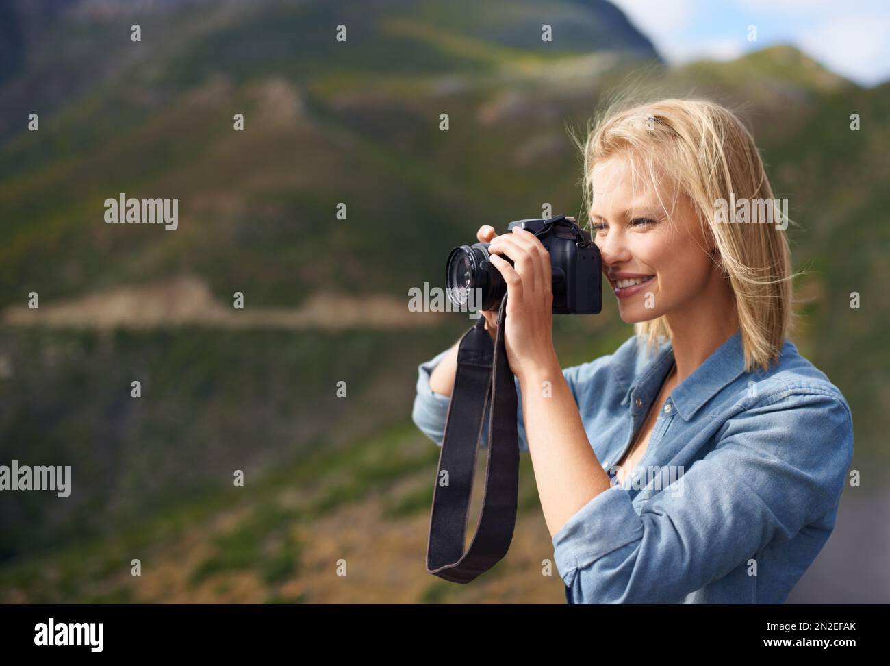 Ich mache einen Schnappschuss ihrer Umgebung. Eine schöne Blondine, die eine Kamera in der Berglandschaft hält. Stockfoto