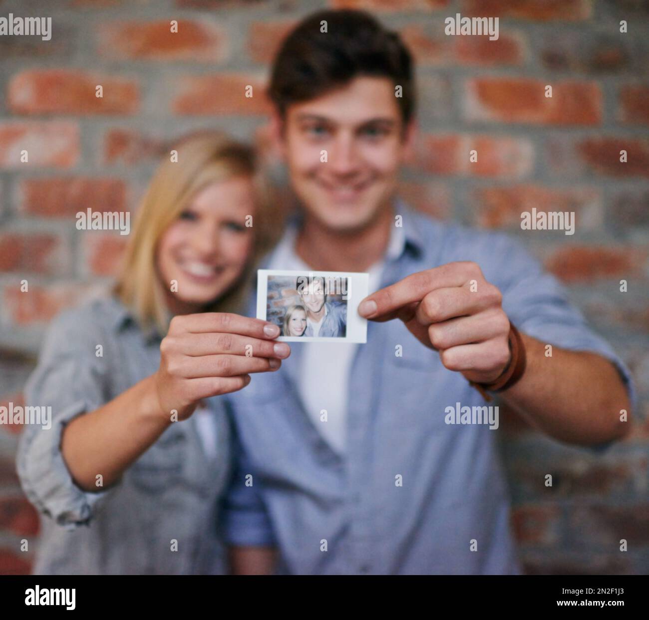 Erinnerungen schaffen. Ein junges Paar, das vor einer Mauer steht und ein Foto vor der Kamera hält. Stockfoto