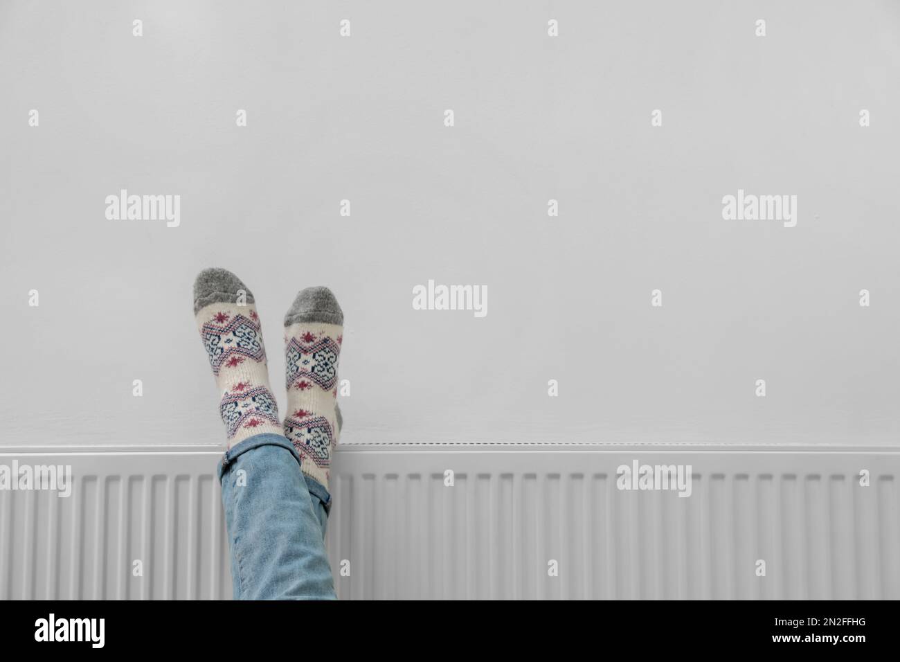 Frau wärmt Beine auf Heizkörper nahe weißer Wand, Nahaufnahme. Platz für Text Stockfoto