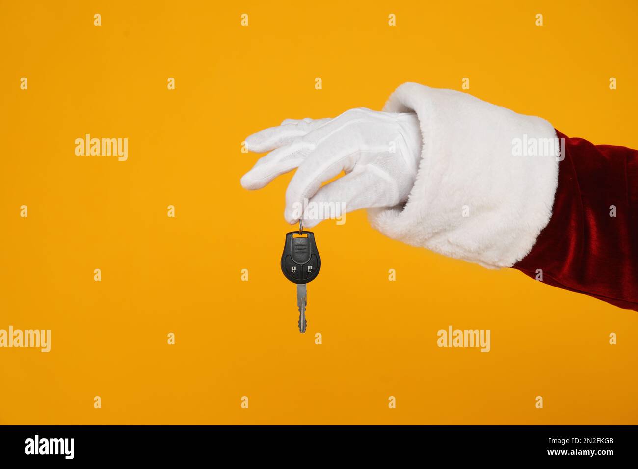Der Weihnachtsmann hält den Autoschlüssel auf gelbem Hintergrund, Nahaufnahme der Hand Stockfoto