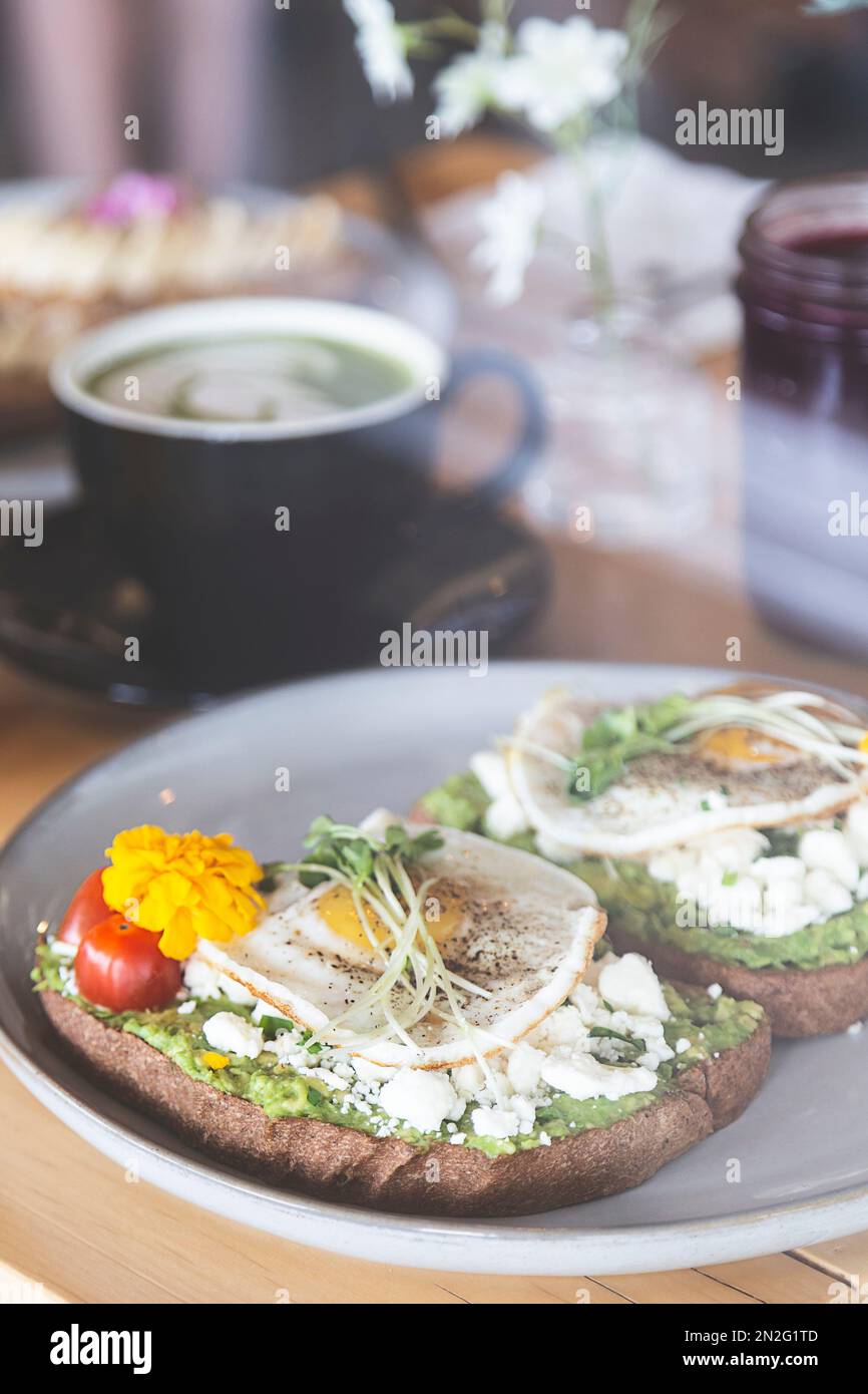 Avocado und Eiertoast mit Bohnensprossen und Tomaten auf einem weißen Teller in einem Frühstücksrestaurant. Vegetarische und gesunde Lebensmittel. Orangensaft Stockfoto