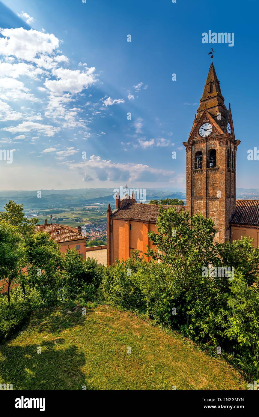 Vertikaler Blick auf den alten Ziegelglockenturm zwischen grünen Bäumen unter blauem Himmel in der Kleinstadt Magliano Alfieri in Piemont, Norditalien. Stockfoto