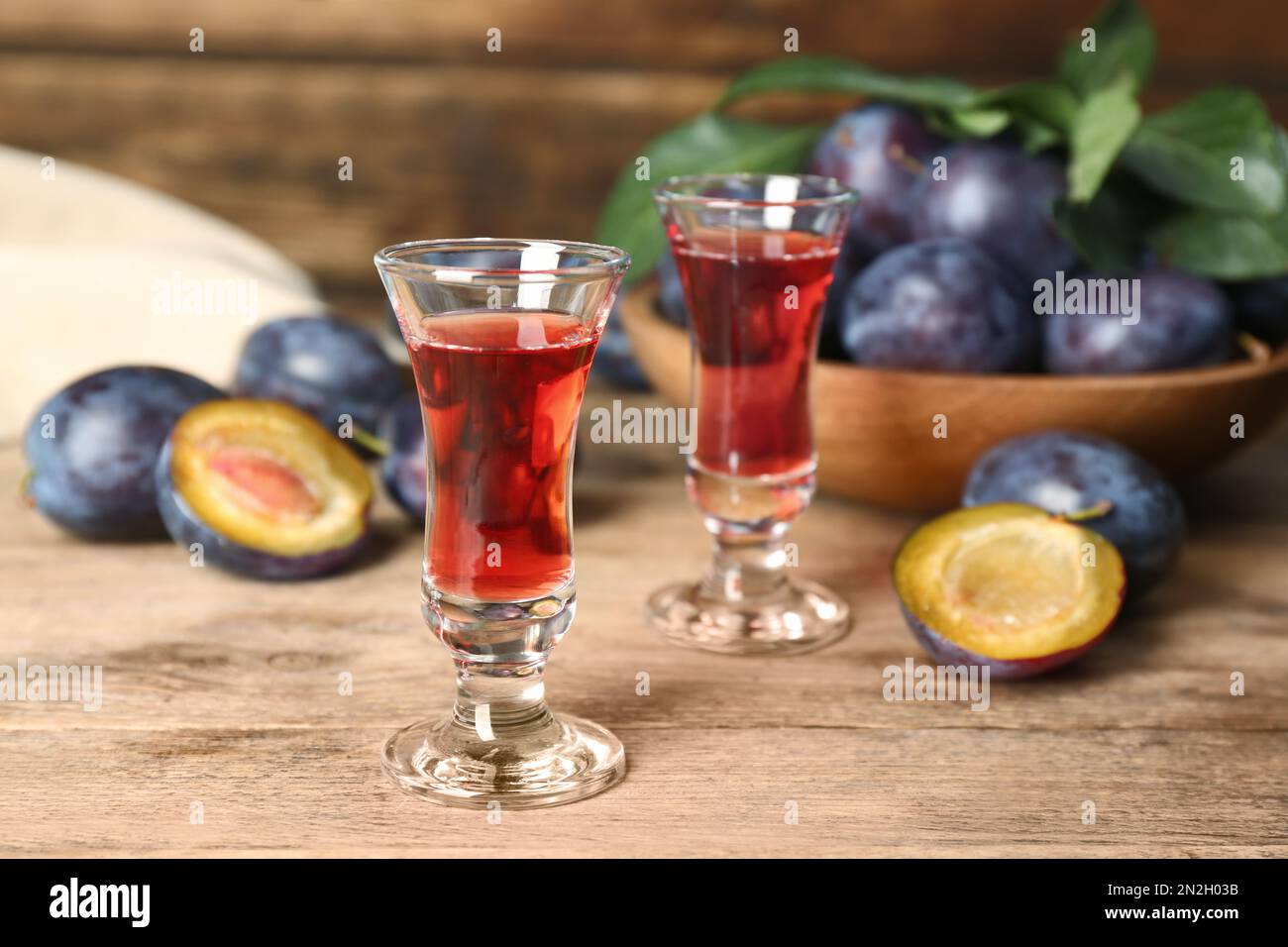 Köstlicher Pflaumenlikör und reife Früchte auf einem Holztisch. Hausgemachtes, starkes alkoholisches Getränk Stockfoto