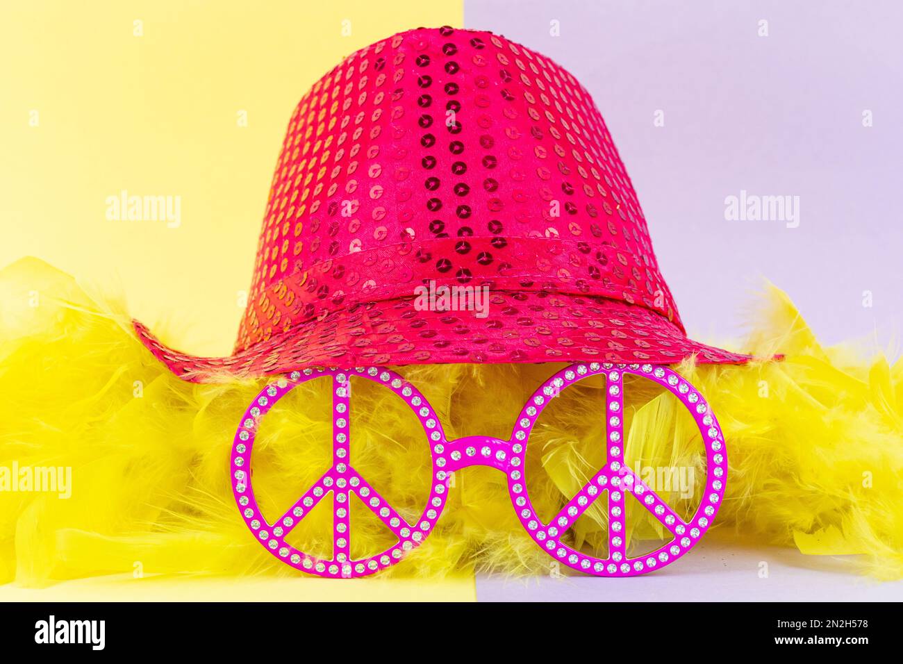 Karnevalskostüm-Accessoires isoliert mit farbigem Hintergrund. Pinkfarbene Mütze mit Pailletten und grüner Brille, roter Nase, gelben Federn und farbigen Bächen Stockfoto