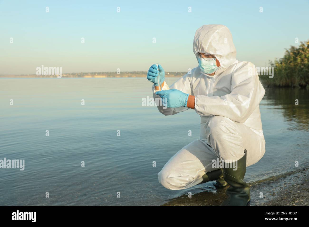 Wissenschaftler im chemischen Schutzanzug mit Reagenzgläser zur Probenentnahme aus dem Fluss zur Analyse Stockfoto