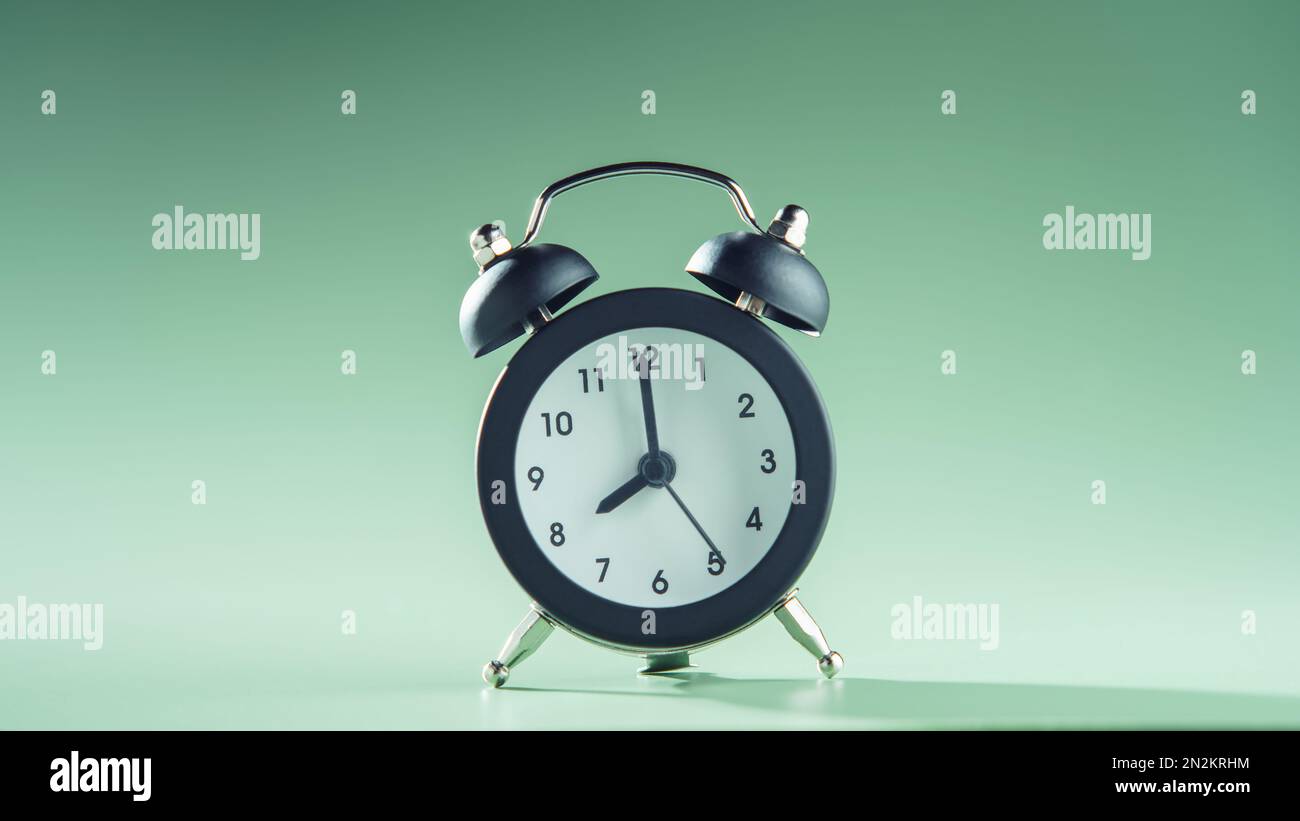 Blaue Uhr zeigt acht Uhr auf grünem Hintergrund. Zeit, Zeitplan, Countdown, Wecker, Zeitplan, Frist, Zeitmanagement, Minimalismus Stockfoto