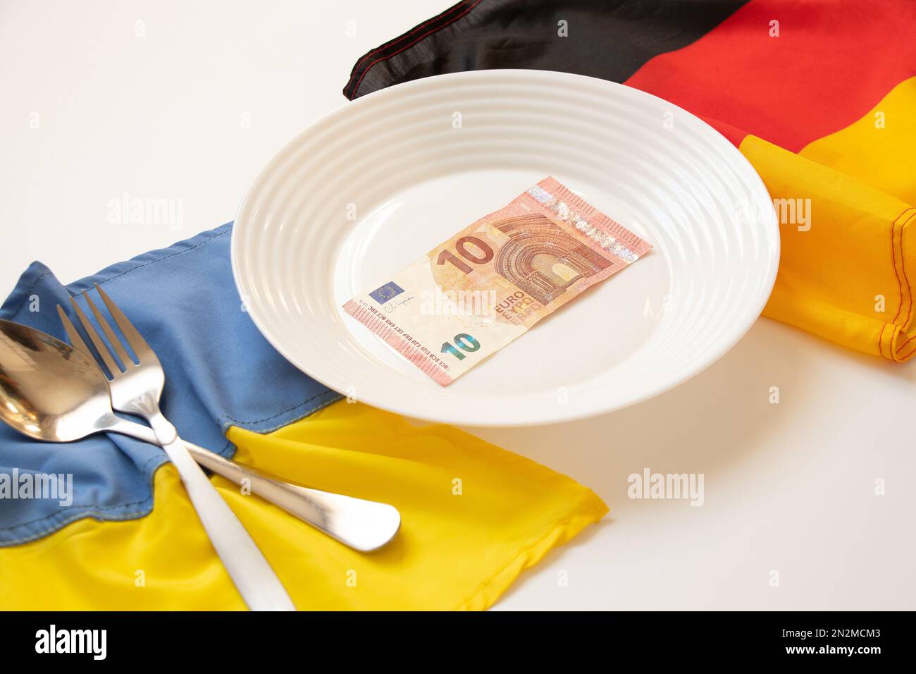 Die Flaggen der Ukraine und Deutschlands liegen in der Nähe eines Tellers mit 10 Euro auf weißem Hintergrund, Wirtschaft und Finanzen, finanzielle Unterstützung für die Ukraine Stockfoto