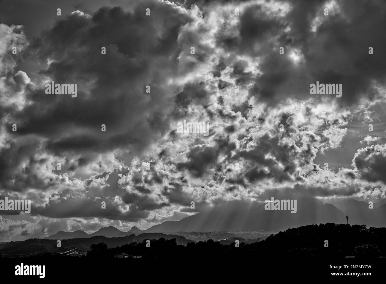 Handyantenne auf einem Hügel im Tal, umgeben von zerklüfteten Bergen unter dramatischen schweren Wolken in Spanien in Schwarz und Weiß Stockfoto