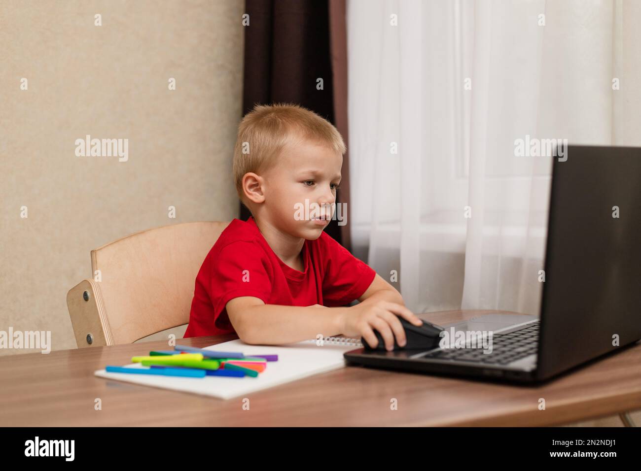 Online-Fernunterricht. Das Kind schaut sich den Laptop genau an und studiert die Zeichenstunde online im Internet. Online-Schule. Stockfoto