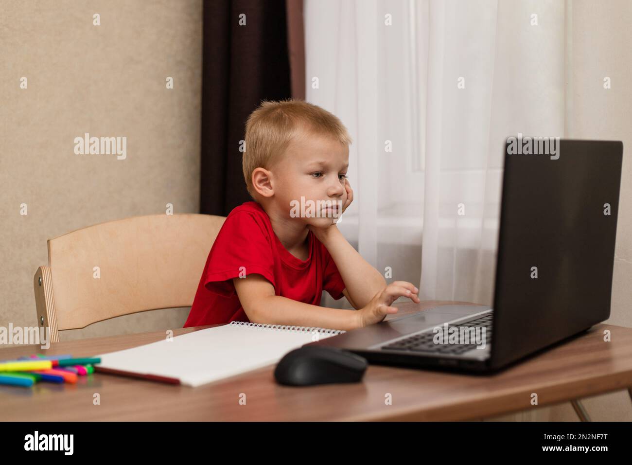 Online-Fernunterricht. Das Kind schaut sich den Laptop genau an und studiert die Zeichenstunde online im Internet. Online-Schule. Stockfoto