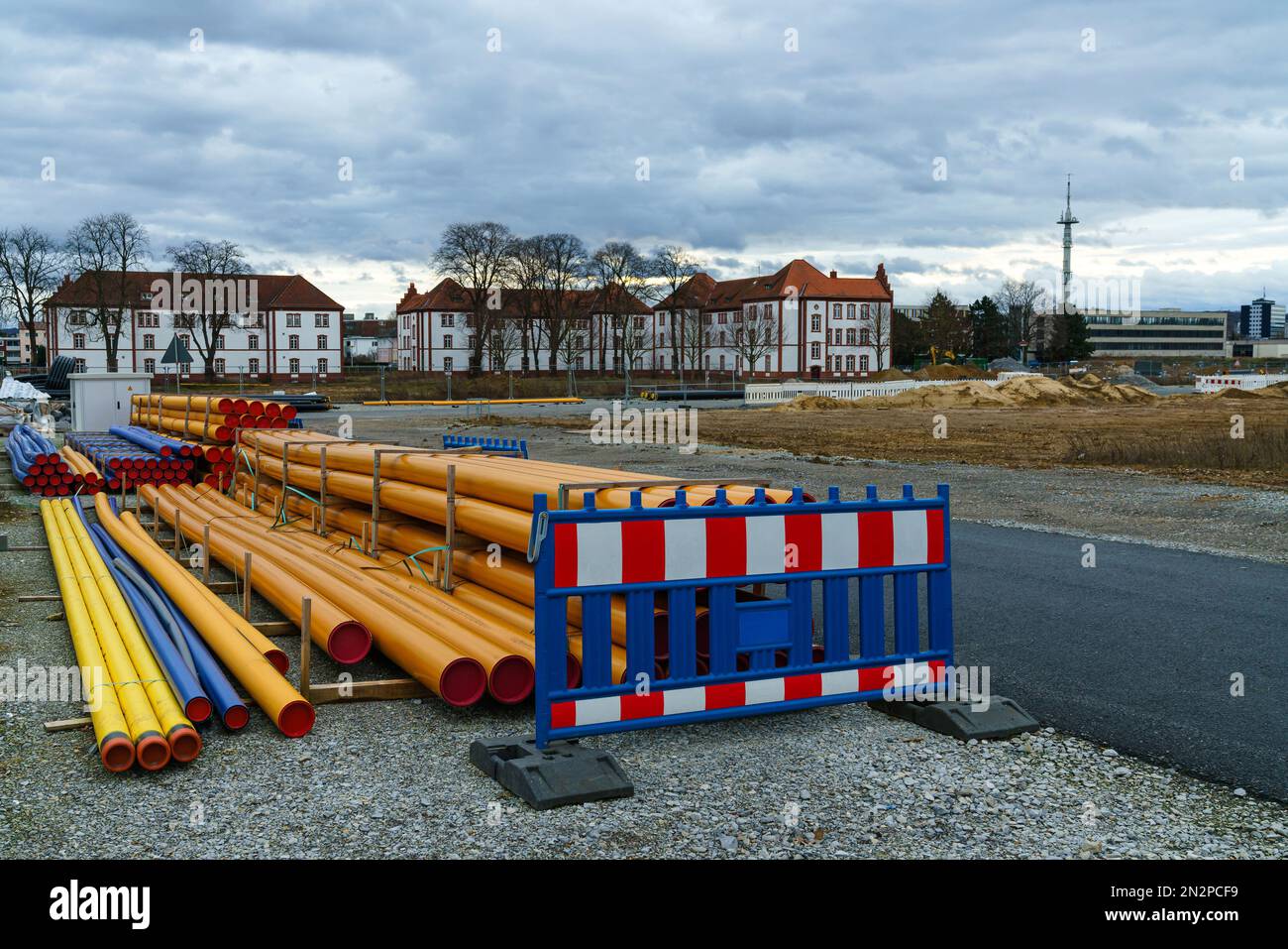 Orangefarbene und blaue Kunststoffrohre und eine tragbare Barriere befinden sich auf einer Baustelle. Gebäude unter einem grauen Himmel im Hintergrund Stockfoto