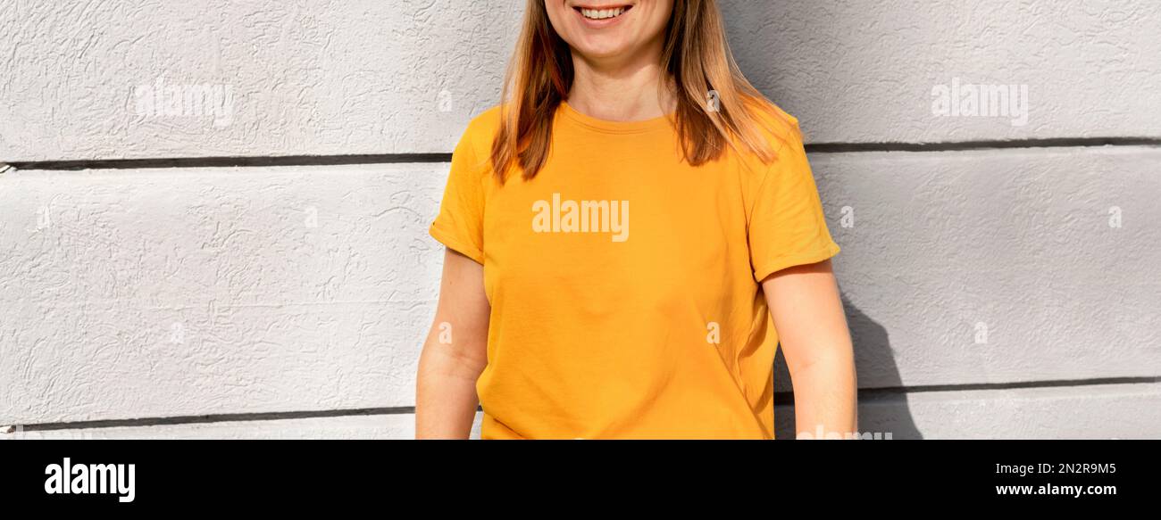 Unerkennbare lächelnde, glückliche blonde Frau im gelb-orangefarbenen T-Shirt auf grauem Hintergrund Mockup-freundlicher Kopierbereich für Design und Text Urban Stockfoto