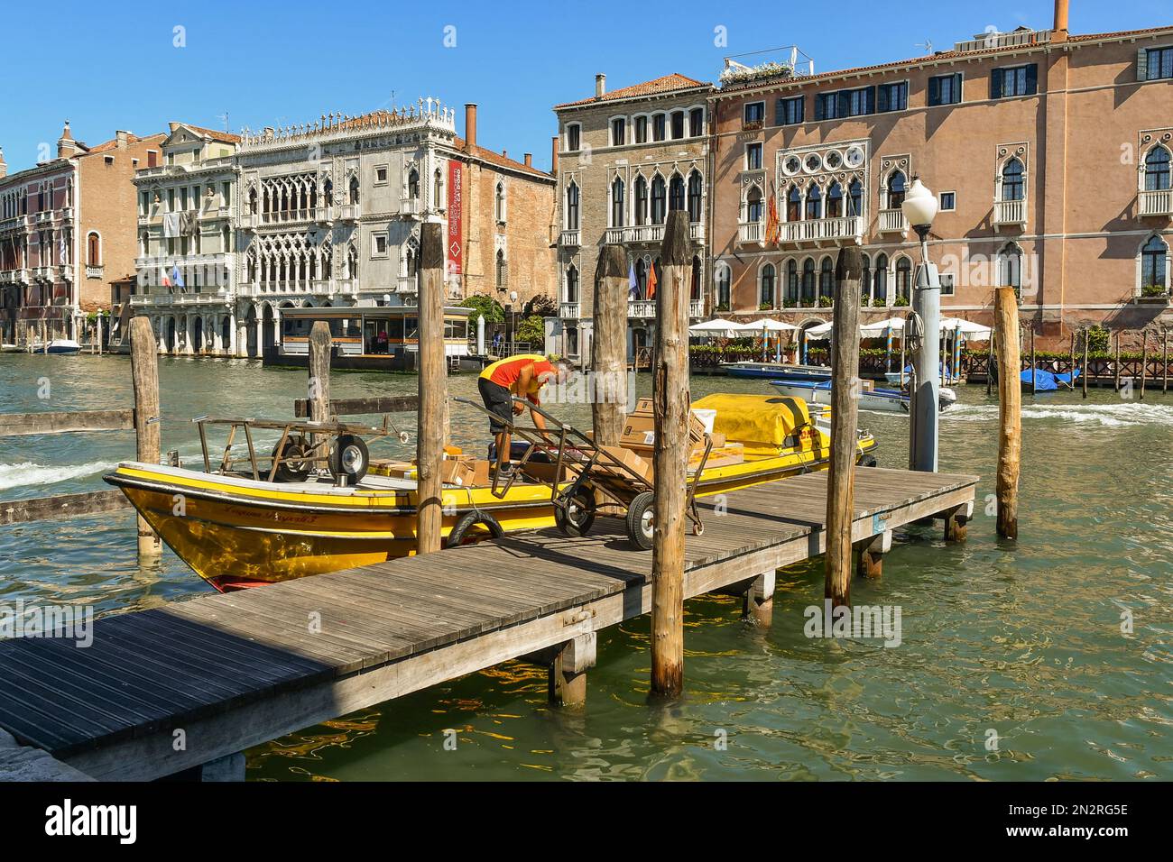 Ein DHL-Kurierboot, das zum Entladen von Kisten auf dem Canale Grande angelegt hat, mit Palästen Cà Sagredo und Cà d'Oro im Hintergrund, Venedig, Venetien, Italien Stockfoto