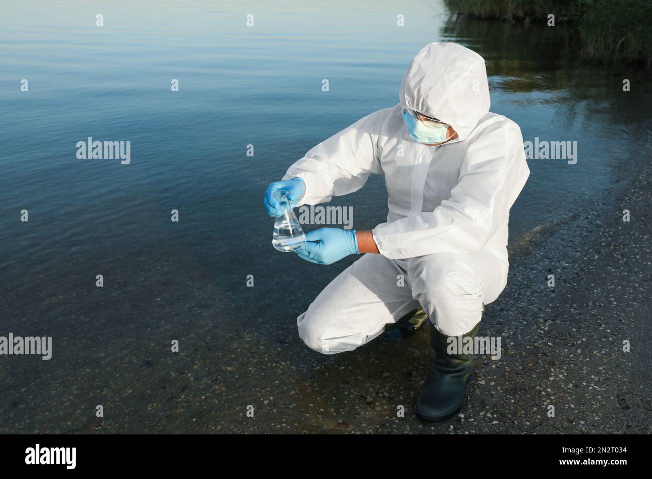 Wissenschaftler im chemischen Schutzanzug mit konischem Kolben, der zur Analyse Proben aus dem Fluss nimmt Stockfoto
