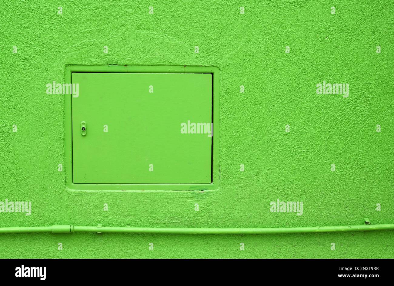 Geschlossene Inspektionsluke über dem Rohr an der Putzwand eines hellgrünen Gebäudes Stockfoto