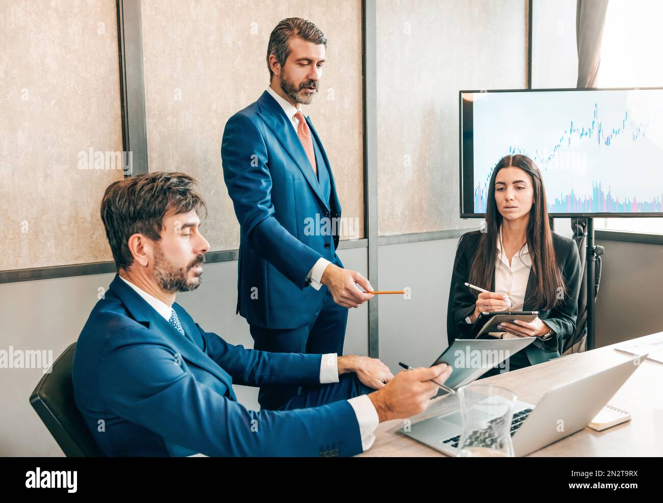 Gruppe von Geschäftsleuten in formeller Kleidung, die sich am Tisch mit einem Laptop versammeln und während des Meetings im Büro mit Karten arbeiten Stockfoto