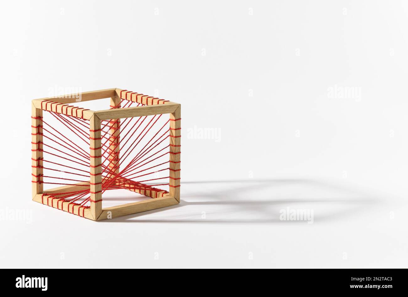 Rote Seile, die an den Holzrahmen eines platonischen Massivwürfels vor weißem Hintergrund gebunden sind Stockfoto