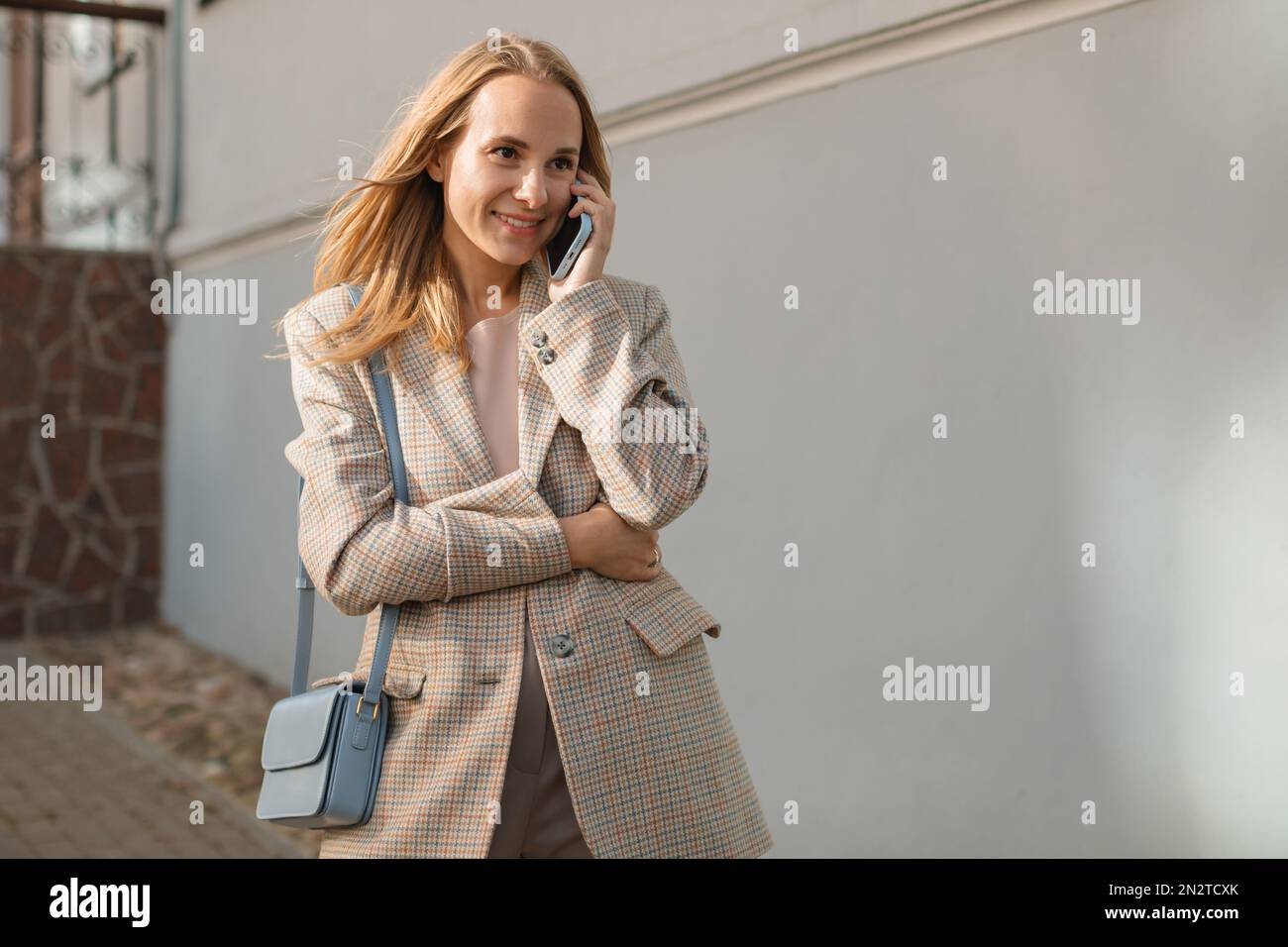 Lächelnde Geschäftsfrau, die auf der Straße steht und mit ihrem Handy, Weißrussland, spricht Stockfoto