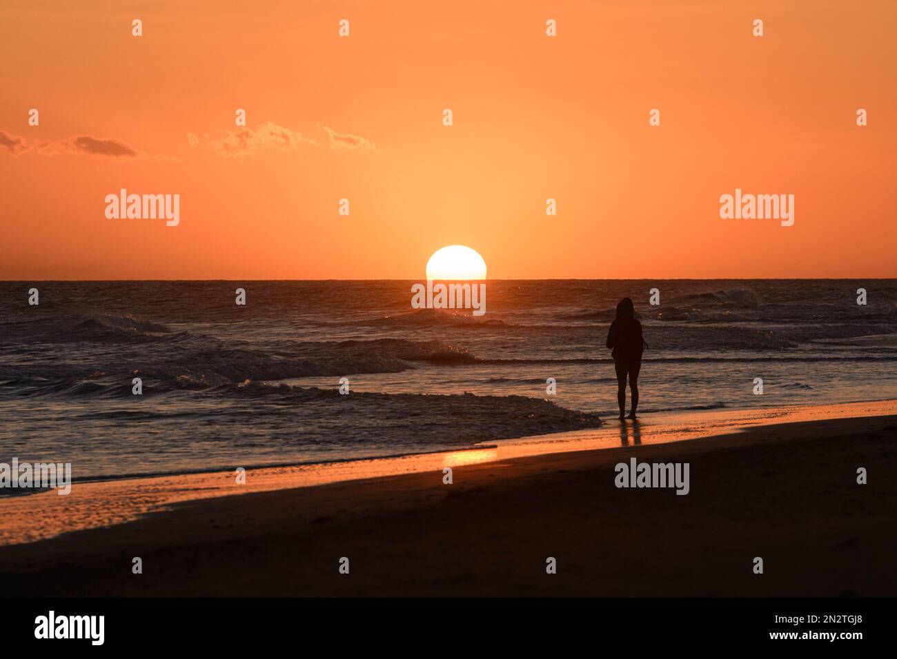 Rückansicht einer Frau, die am Strand steht und das Meer bei Sonnenuntergang betrachtet, Maspalomas Strand, Gran Canaria, Kanarische Inseln, Spanien Stockfoto