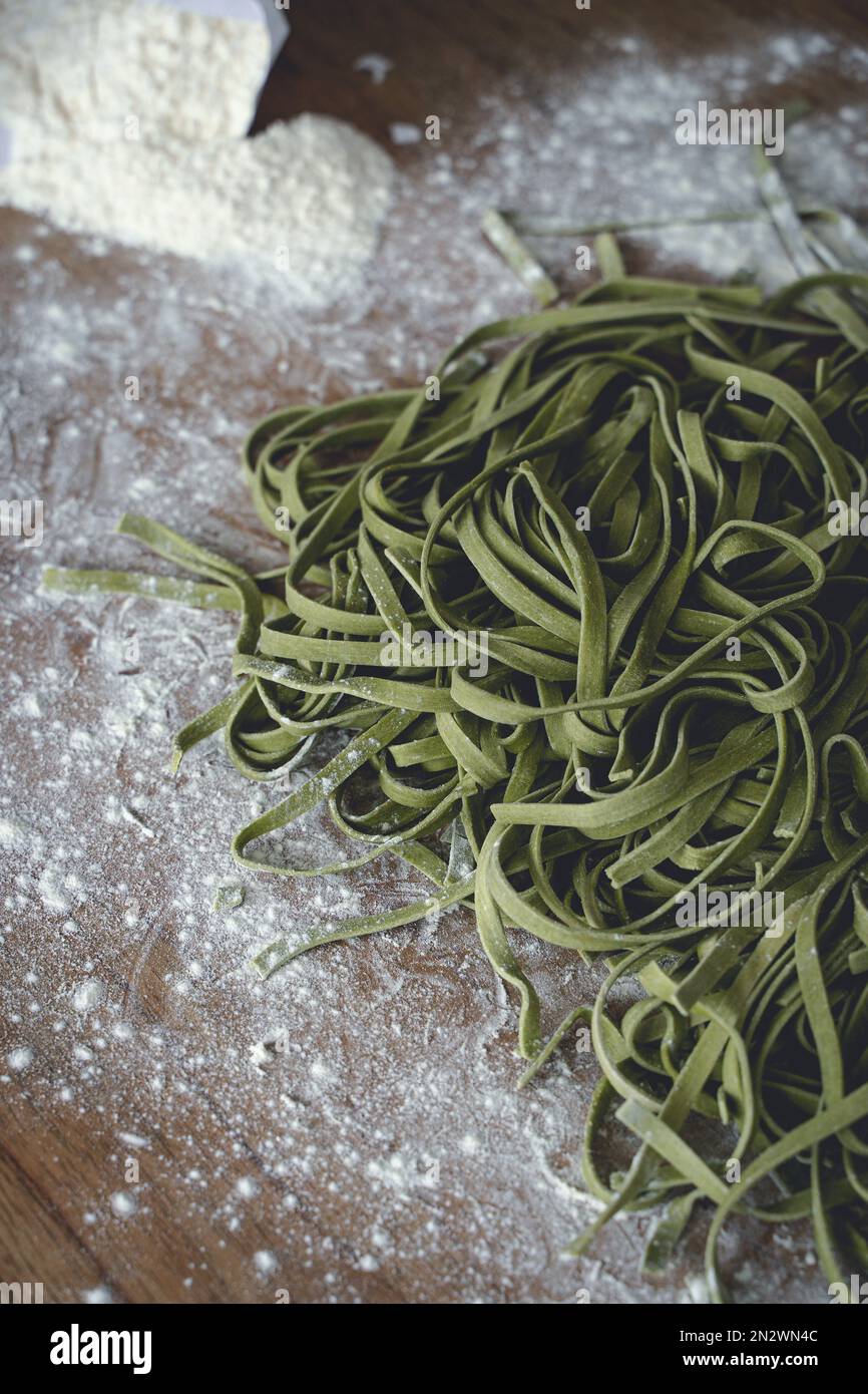 Frische Pasta. Hausgemachte italienische rohe Fettuccine-Pasta mit Spinat auf Holztisch. Hochwertiges Foto Stockfoto