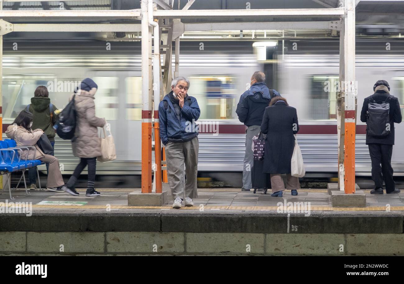 Passagiere, die auf dem Bahnsteig warten, um nachts zum Zug der Tobu-Linie zu gelangen. Ein älterer Mann sieht betrunken aus und wartet, während ein Zug vorbeifährt. Stockfoto