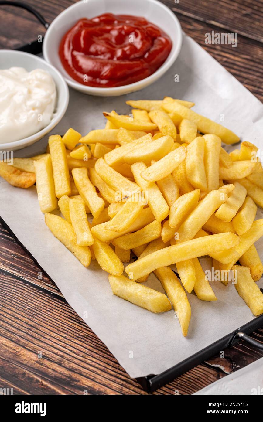 Goldene Pommes Frites mit Ketchup und Mayonnaise auf einem Holztisch Stockfoto