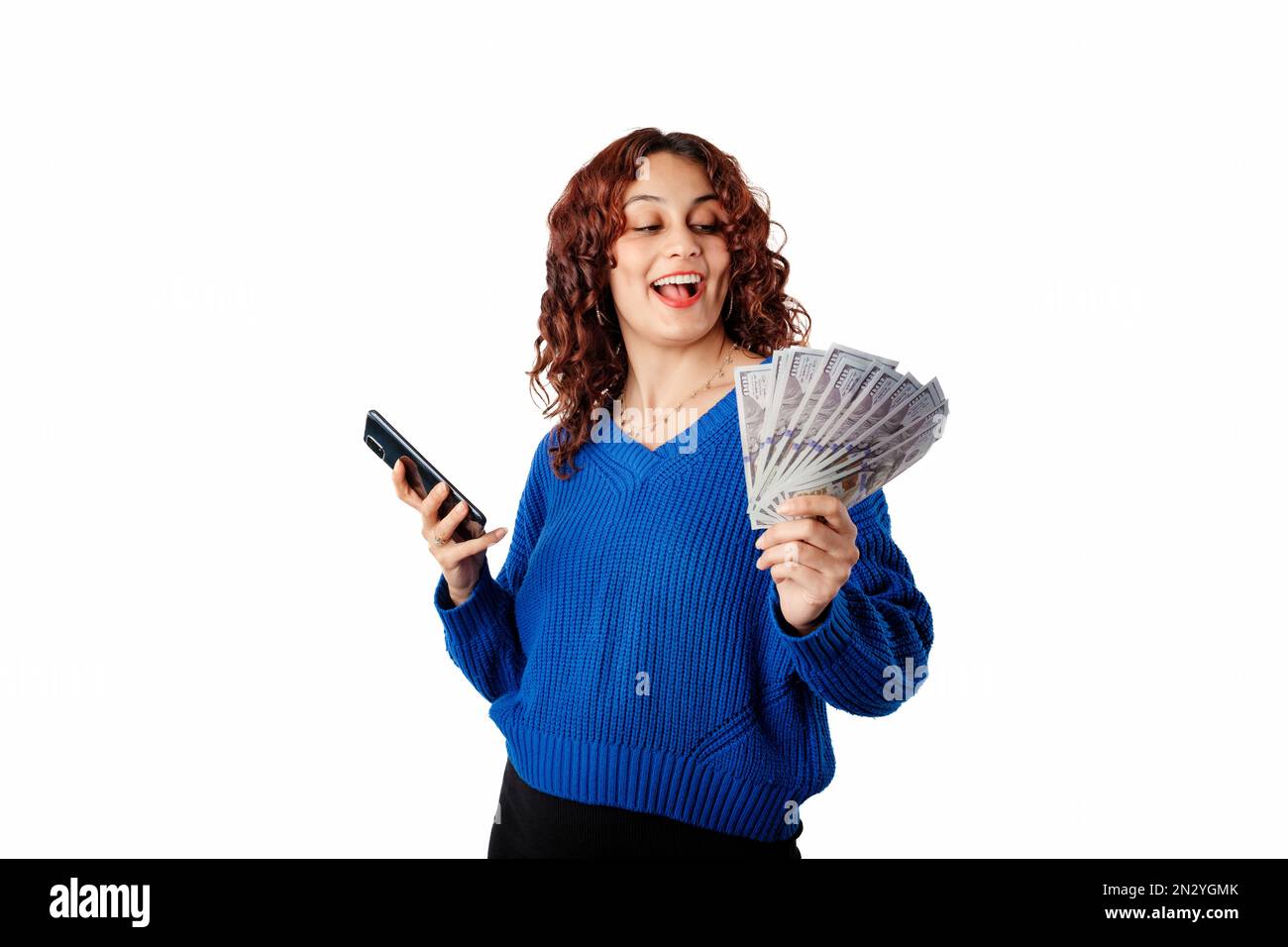 Porträt einer jungen Frau mit blauem Strickpullover, die isoliert auf weißem Hintergrund steht und Geldscheine mit dem Handy hält. Bunc wird angezeigt Stockfoto