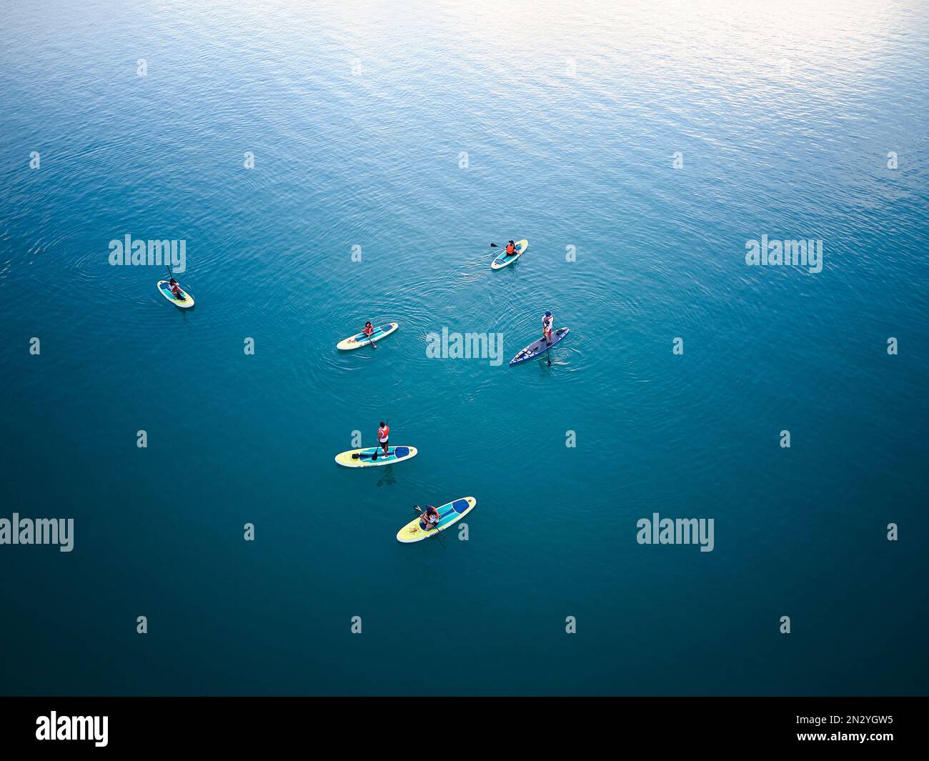 Luftdrohnenaufnahme von oben nach unten von einer Gruppe von Personen, die auf Stand-Up-Paddle-Boards SUP im blauen Meerwasser rudern. Stockfoto